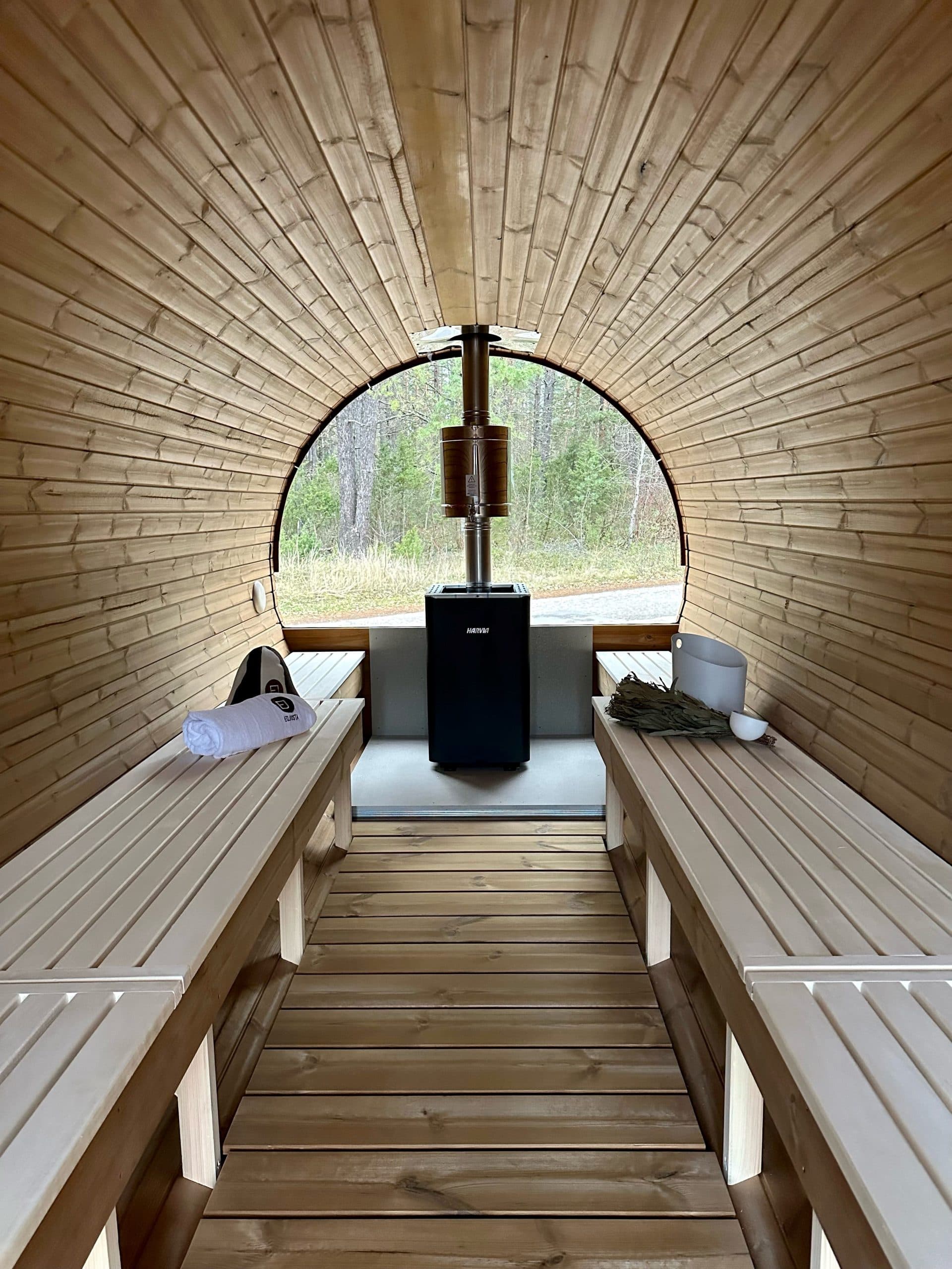 Inside a mobile sauna showing timber benches, heater and panoramic window